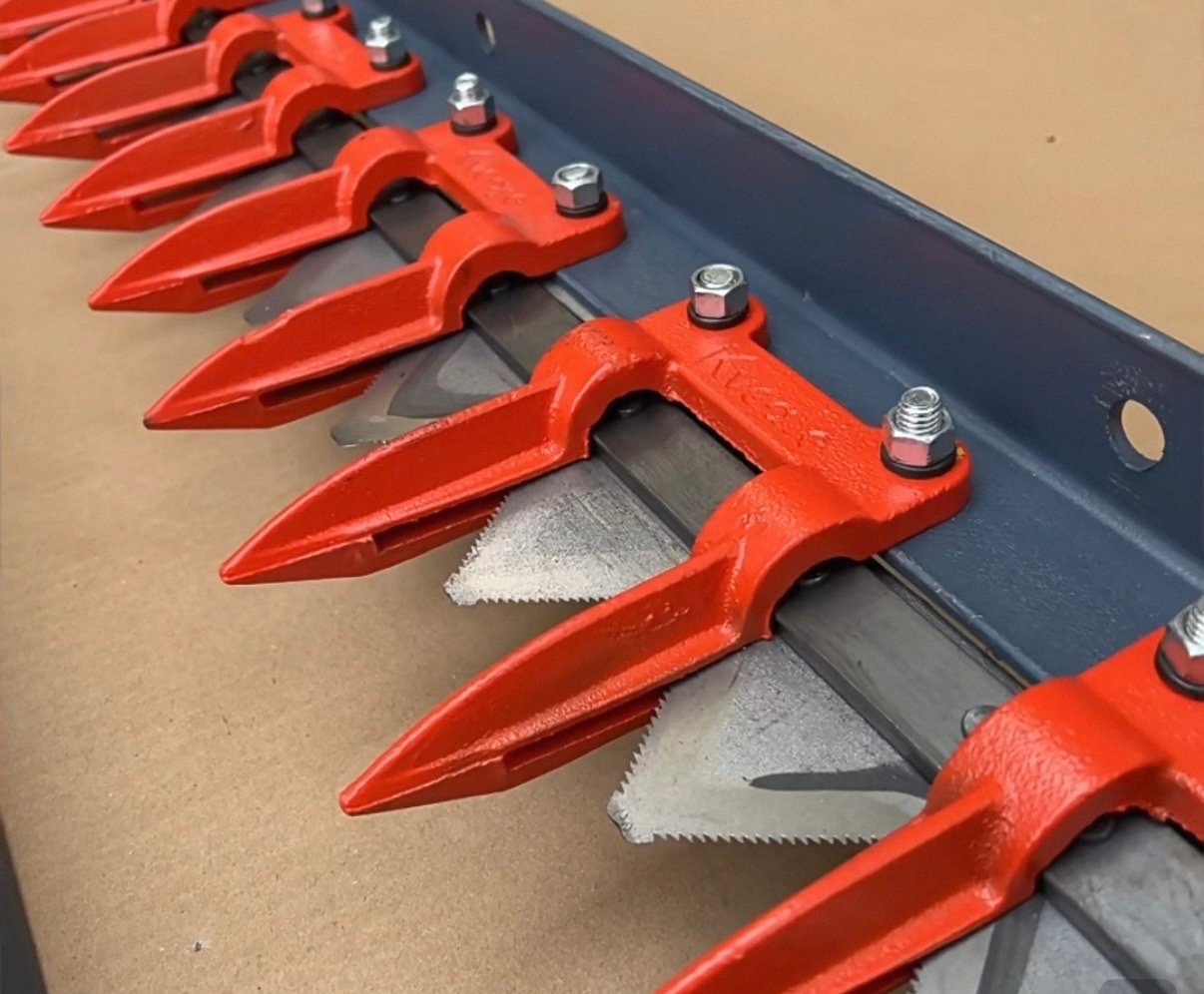 Close-up of combine harvester cutter bar with red knife guards and serrated blades